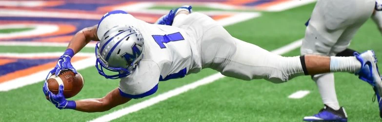 Ein American-Football-Spieler mit helmförmiger Ausrüstung springt waagerecht in der Luft, um den Ball abzufangen
